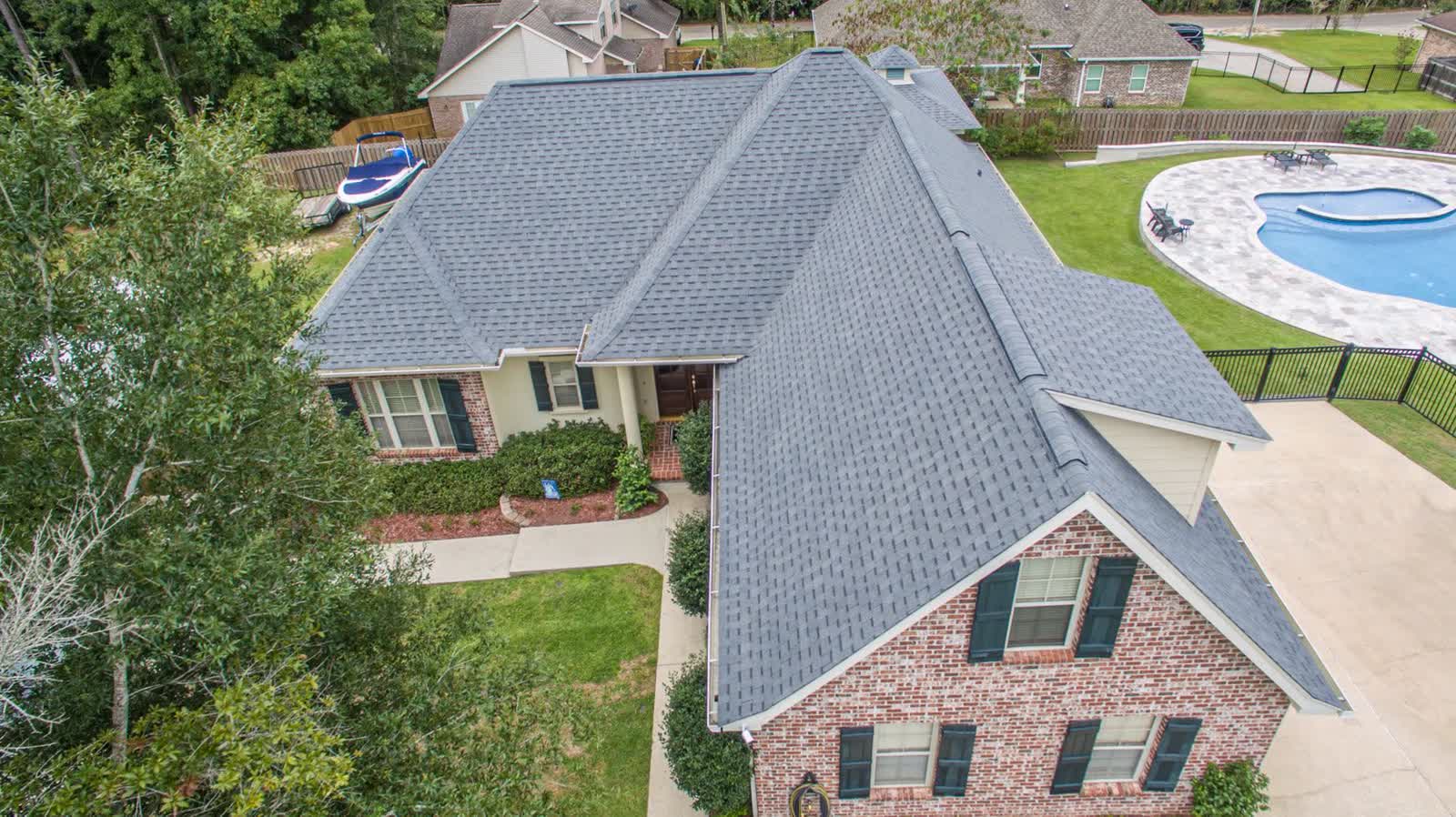 Completed architectural shingle roof replacement on a brick home in Diamondhead, Mississippi, seen from above with the pool and yard beyond